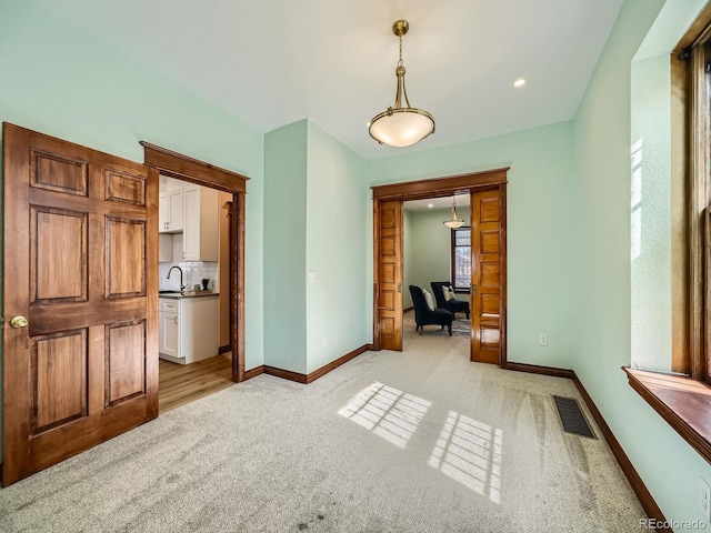 interior space with baseboards, a sink, visible vents, and light colored carpet