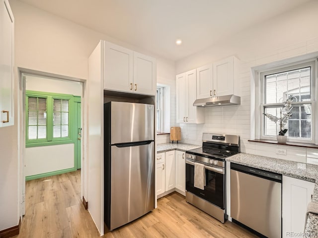 kitchen featuring under cabinet range hood, stainless steel appliances, white cabinets, decorative backsplash, and light wood finished floors