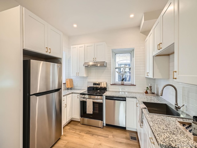 kitchen featuring stainless steel appliances, light wood-style floors, white cabinetry, a sink, and under cabinet range hood