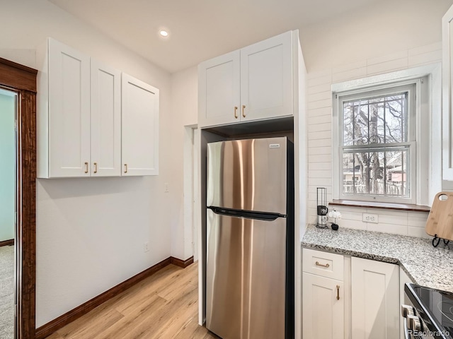 kitchen with light wood finished floors, tasteful backsplash, baseboards, white cabinets, and freestanding refrigerator