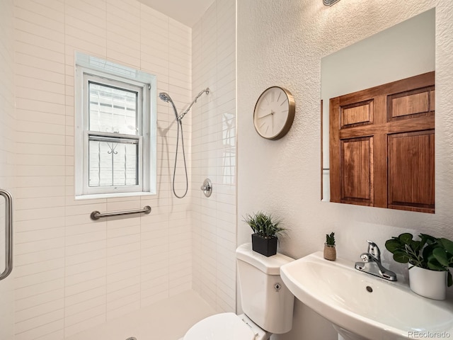 bathroom featuring a textured wall, tiled shower, a sink, and toilet