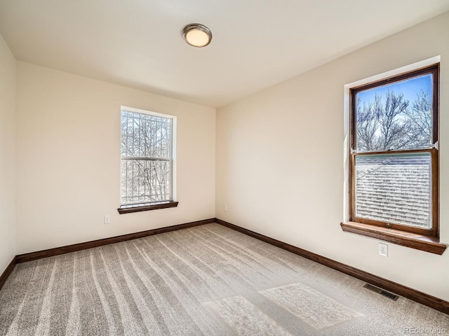 empty room with carpet, visible vents, and baseboards