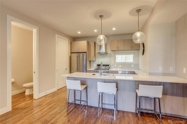 kitchen with light brown cabinets, kitchen peninsula, hanging light fixtures, appliances with stainless steel finishes, and light hardwood / wood-style floors