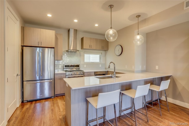 kitchen with sink, kitchen peninsula, stainless steel appliances, wall chimney exhaust hood, and light brown cabinets