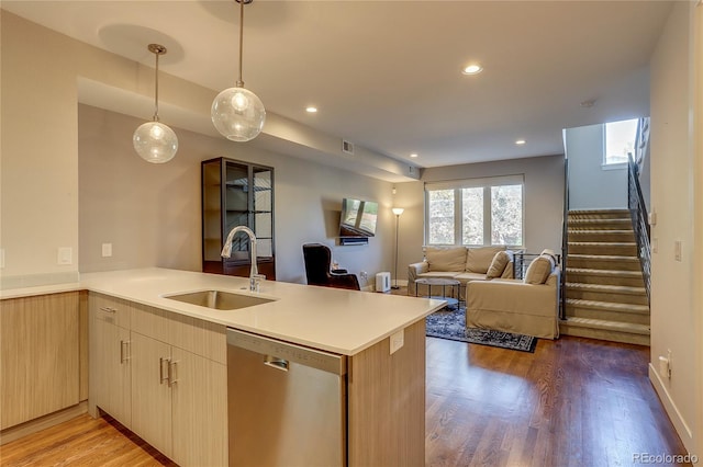 kitchen with hanging light fixtures, kitchen peninsula, wood-type flooring, sink, and stainless steel dishwasher