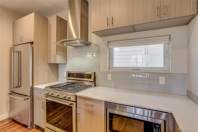 kitchen featuring wall chimney range hood, stainless steel appliances, light brown cabinetry, and light wood-type flooring