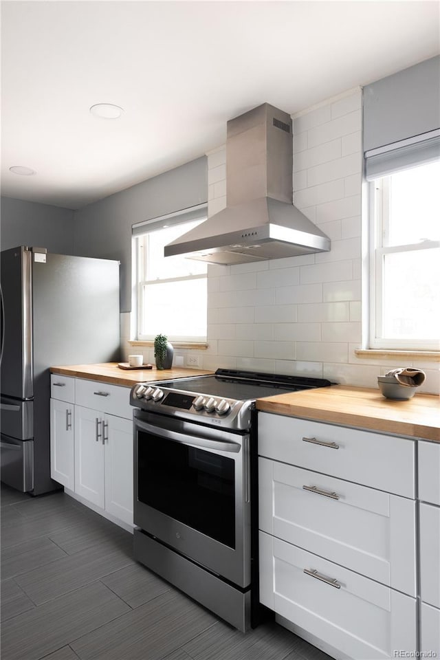 8240 Grandview Ave, Arvada, CO 80002 - kitchen with wood counters, wall chimney exhaust hood, appliances with stainless steel finishes, white cabinetry, and decorative backsplash