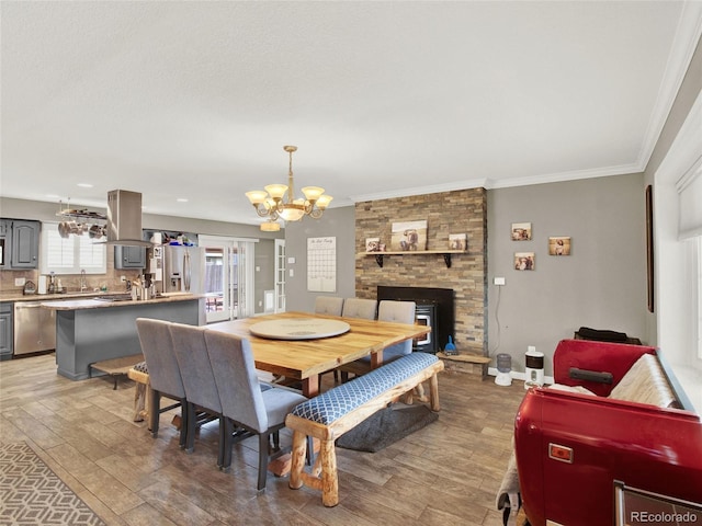 dining room with ornamental molding, baseboards, a chandelier, light wood finished floors, and a fireplace