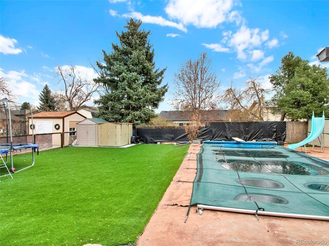 view of yard featuring a fenced in pool, a trampoline, an outbuilding, a fenced backyard, and a storage unit