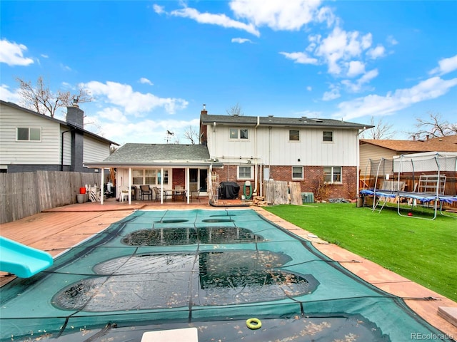 view of pool featuring a water slide, a fenced in pool, a trampoline, a fenced backyard, and a lawn