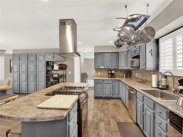 kitchen with a sink, tasteful backsplash, gray cabinetry, stainless steel appliances, and island exhaust hood