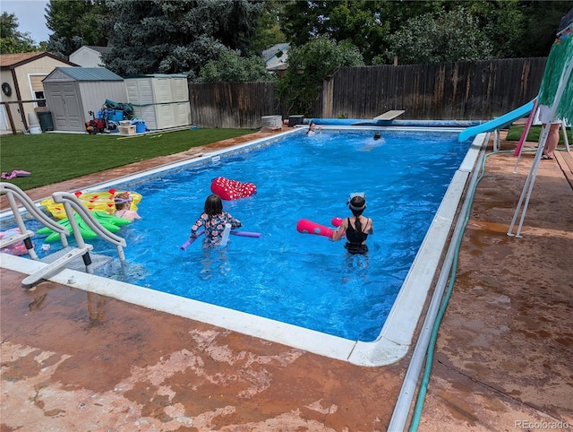 view of pool featuring a water slide, an outbuilding, a fenced backyard, a storage unit, and a yard