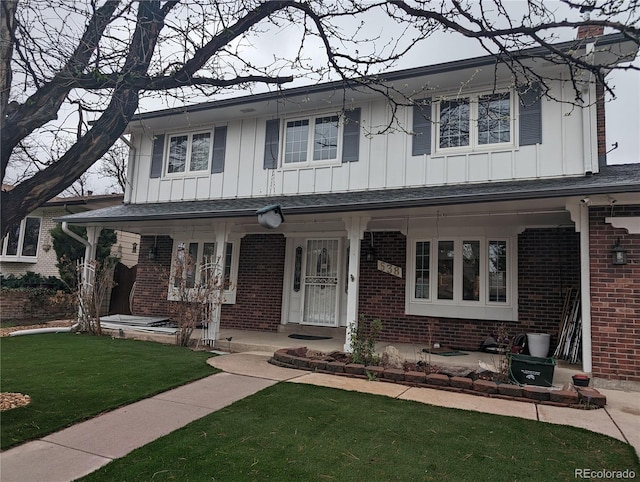 view of front of house featuring brick siding, board and batten siding, covered porch, and a front yard