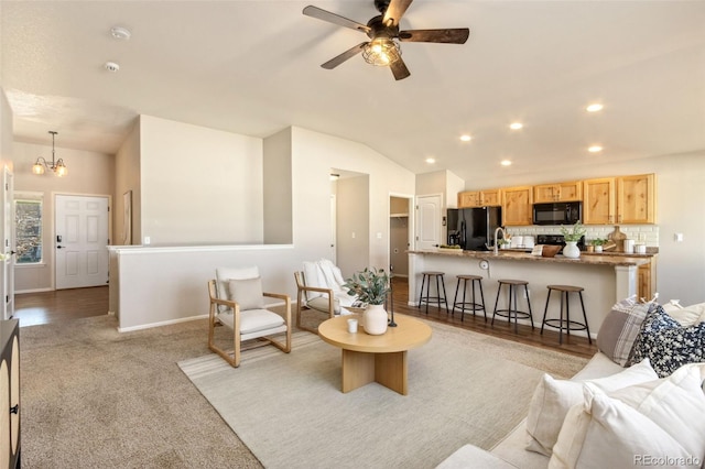 living room with ceiling fan with notable chandelier, light hardwood / wood-style floors, and vaulted ceiling