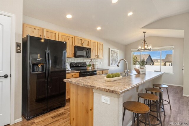 kitchen with an island with sink, black appliances, lofted ceiling, and light hardwood / wood-style floors