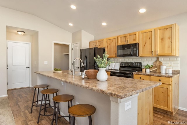 kitchen featuring backsplash, dark wood-type flooring, black appliances, vaulted ceiling, and an island with sink