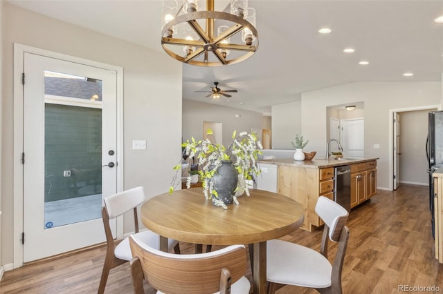 dining area featuring sink, ceiling fan with notable chandelier, lofted ceiling, and light wood-type flooring