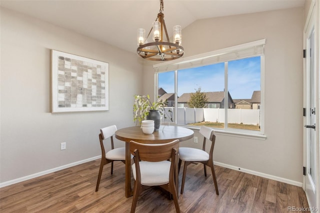 dining space with hardwood / wood-style floors, vaulted ceiling, and an inviting chandelier