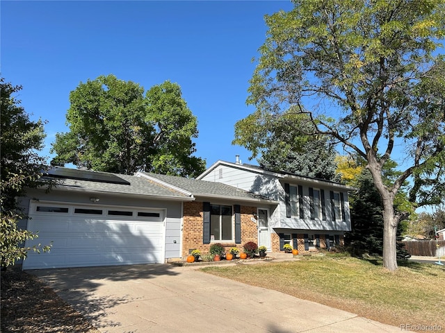 tri-level home featuring a front yard, a garage, and solar panels