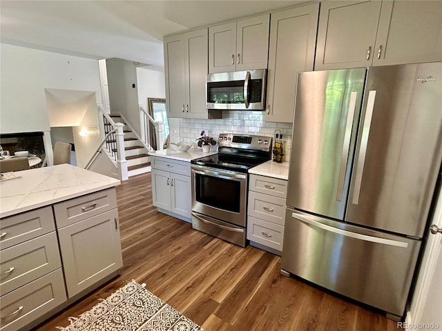 kitchen with light stone counters, tasteful backsplash, gray cabinetry, stainless steel appliances, and dark hardwood / wood-style floors