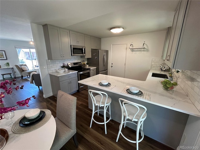 kitchen with a breakfast bar area, stainless steel appliances, dark wood-type flooring, and kitchen peninsula