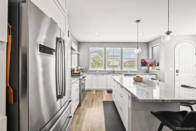 15547 W Vassar Ave, Lakewood, CO 80228 - kitchen with appliances with stainless steel finishes, light wood-style floors, a breakfast bar, white cabinets, and light stone counters