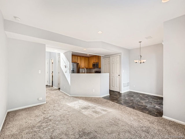 unfurnished living room featuring sink, dark carpet, and a notable chandelier