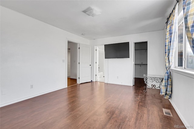 unfurnished bedroom featuring connected bathroom, a closet, a walk in closet, and dark hardwood / wood-style floors