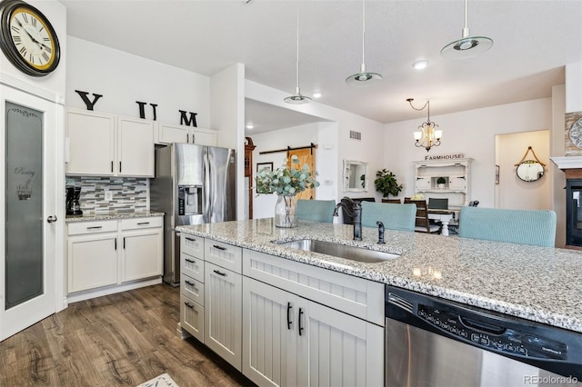 4293 Clover Ln, Brighton, CO 80601 - kitchen featuring appliances with stainless steel finishes, a sink, dark wood-style floors, decorative light fixtures, and light stone counters