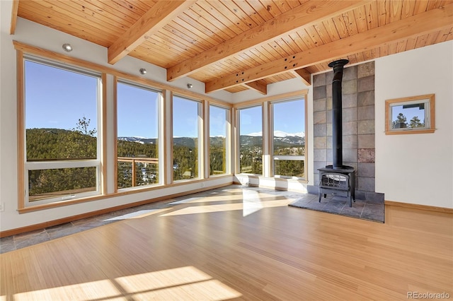 unfurnished living room featuring wood ceiling, a wood stove, light hardwood / wood-style flooring, and beamed ceiling