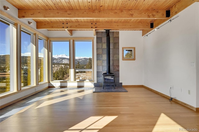 unfurnished living room with wood ceiling, beamed ceiling, a wood stove, light wood-type flooring, and a mountain view