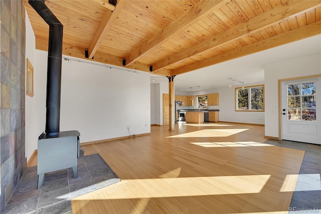 unfurnished living room with a wood stove, beam ceiling, wood ceiling, and light wood-type flooring