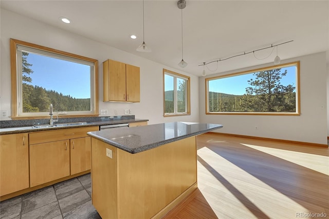 kitchen featuring dark stone countertops, a center island, sink, track lighting, and light brown cabinetry