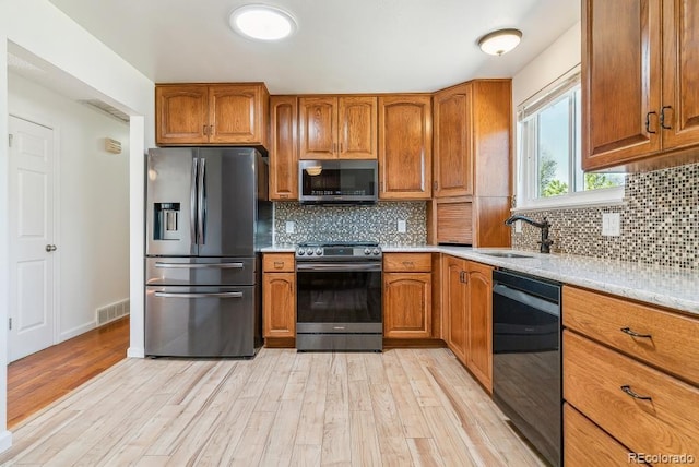 kitchen featuring appliances with stainless steel finishes, light wood-type flooring, brown cabinets, and visible vents