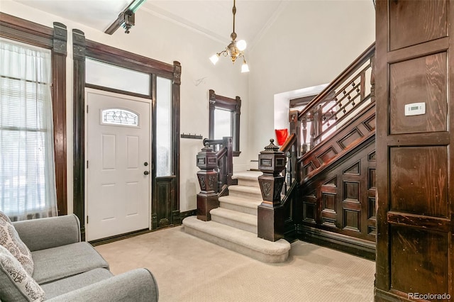 foyer with crown molding, a notable chandelier, and light colored carpet