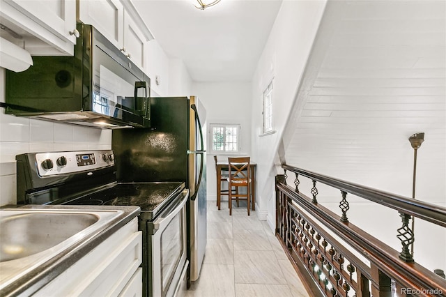 kitchen featuring stainless steel electric stove, white cabinets, light tile patterned floors, and backsplash