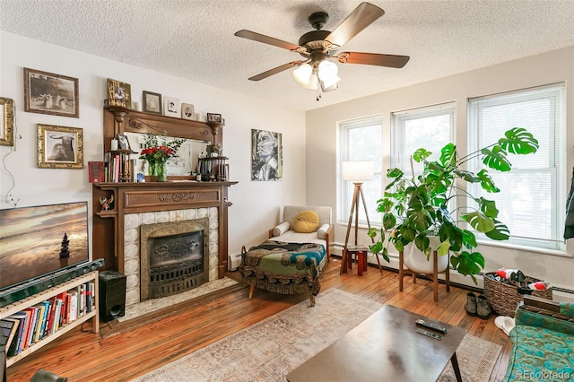 sitting room with baseboard heating, hardwood / wood-style floors, a textured ceiling, a fireplace, and ceiling fan