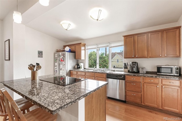 kitchen with light hardwood / wood-style flooring, hanging light fixtures, stainless steel appliances, sink, and a kitchen bar