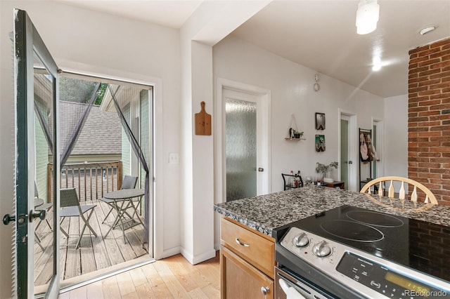 kitchen featuring range with electric stovetop, light hardwood / wood-style flooring, and dark stone countertops