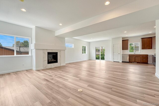 unfurnished living room with sink, a high end fireplace, and light hardwood / wood-style floors