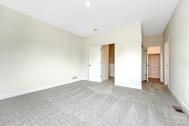 unfurnished bedroom featuring a walk in closet, light colored carpet, and a closet