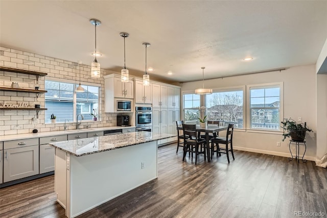 kitchen with light stone counters, sink, pendant lighting, a kitchen island, and stainless steel microwave