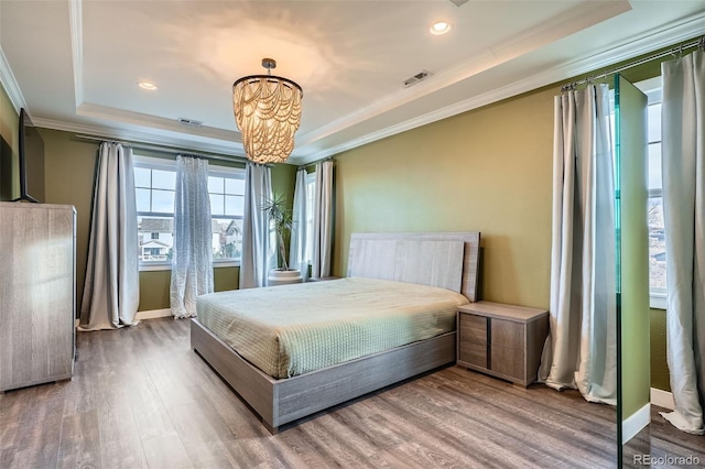 bedroom with a tray ceiling, crown molding, hardwood / wood-style flooring, and a notable chandelier