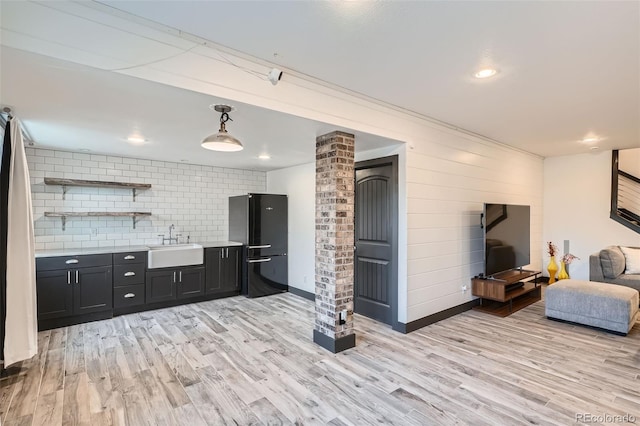 kitchen with sink, hanging light fixtures, black fridge, light hardwood / wood-style flooring, and decorative backsplash