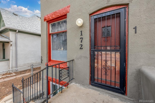 entrance to property with stucco siding and a shingled roof