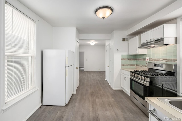 kitchen with visible vents, stainless steel range with gas stovetop, freestanding refrigerator, under cabinet range hood, and backsplash