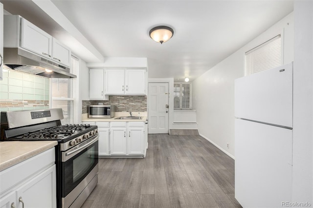 kitchen featuring under cabinet range hood, wood finished floors, stainless steel appliances, white cabinets, and light countertops