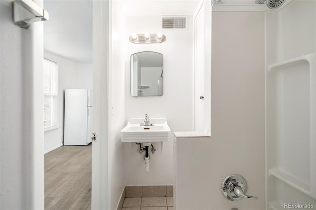 bathroom featuring wood finished floors, baseboards, visible vents, a sink, and a shower