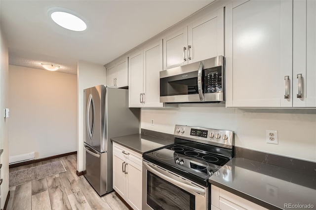 kitchen featuring dark countertops, baseboards, white cabinets, light wood finished floors, and stainless steel appliances