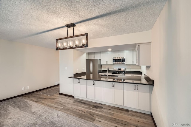 kitchen with dark countertops, appliances with stainless steel finishes, a sink, a textured ceiling, and wood finished floors
